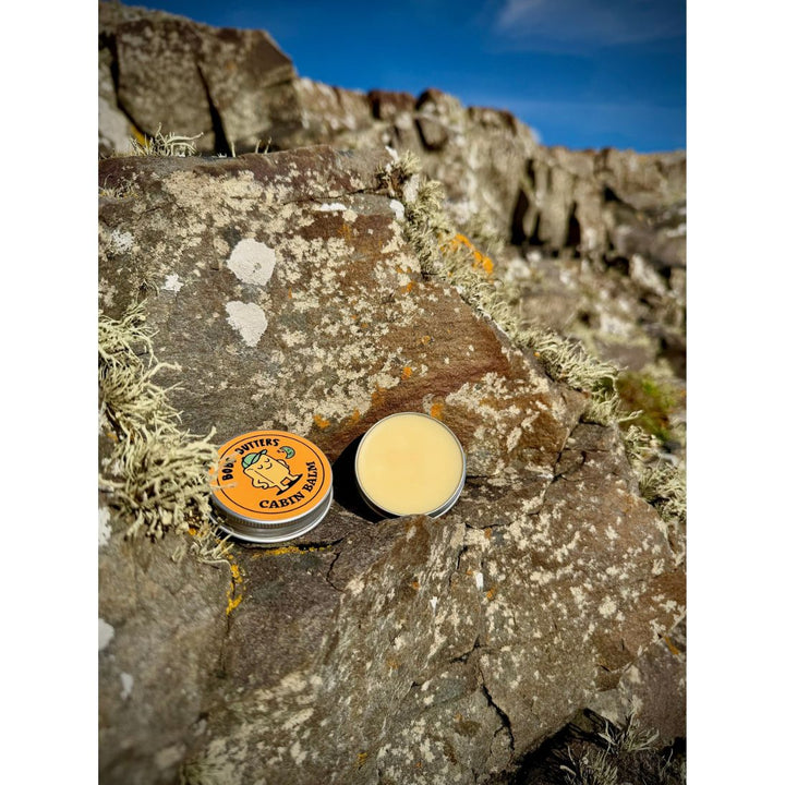Small round opened metal tin of lip balm placed on a rocky outdoor surface under a blue sky. 
