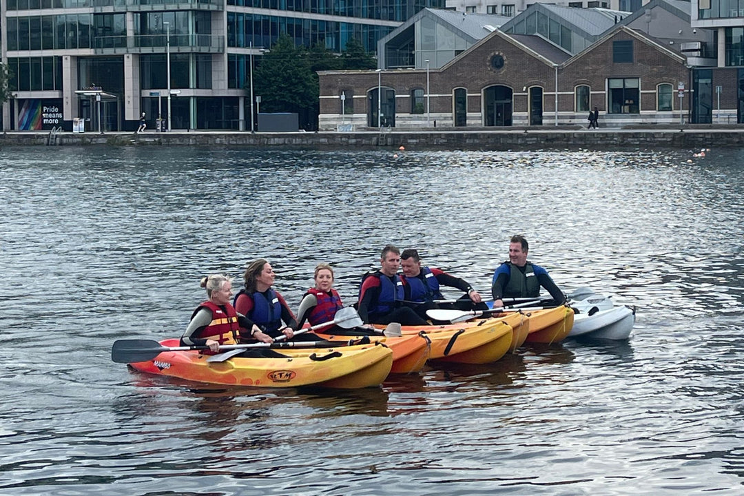 Group of people kayaking on a body of water with buildings in the background