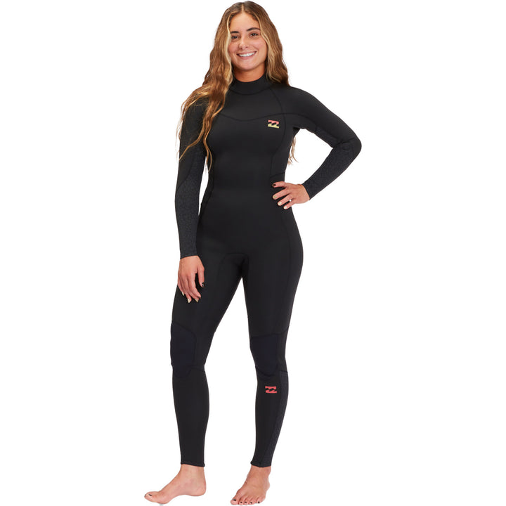 A woman standing and posing in a black full-sleeve Billabong womens wetsuit with a back zip.